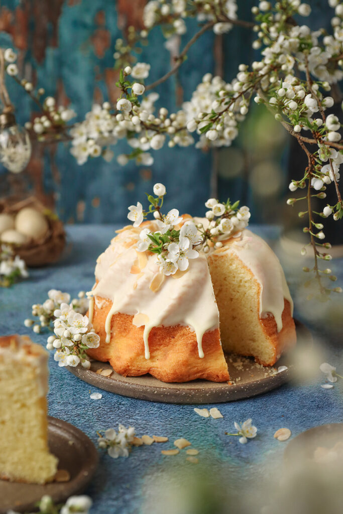 babka wielkanocna polana polewa z białej czekolady i ozdobiona wiosennymi kwiatami. Żółta babka na niebieskim tle