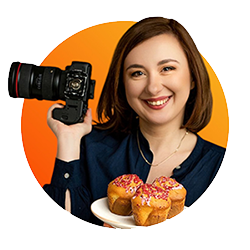 fotograf trzymający w jednej ręce aparat fotograficzny a w drugiej talerz z babeczkami