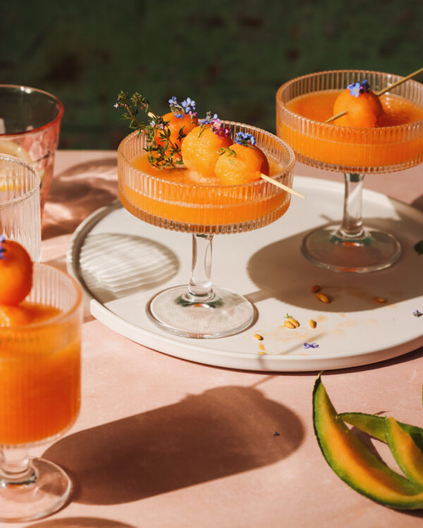 pomarańczowe drinki w kieliszkach ozdobione kwiatami i kulkami melona, drinki z melonem, letnie drinki, fotografia kulinarna, fotograf kulinarny, pyszny kadr kinga ciszewska