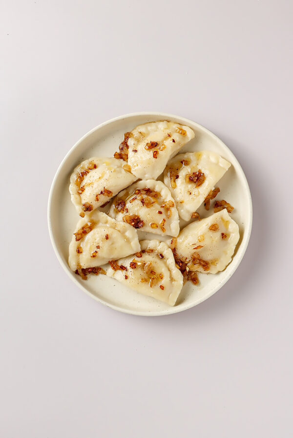 Ruskie pierogi ze skwarkami podane na talerzu. jest to przykład fotografii produktowej dla cateringu, restauracji oferującej swoje dania w aplikacjach do zamawiania jedzenia np. uber eats czy glovo